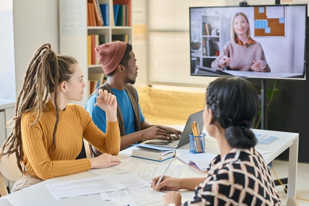 A diverse group of students participating in an online class through video conference, guided by their professor.