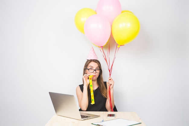 A female office worker is shown joyfully holding up a university diploma in her office cubicle, with balloons and congratulatory notes decorating her workspace.
