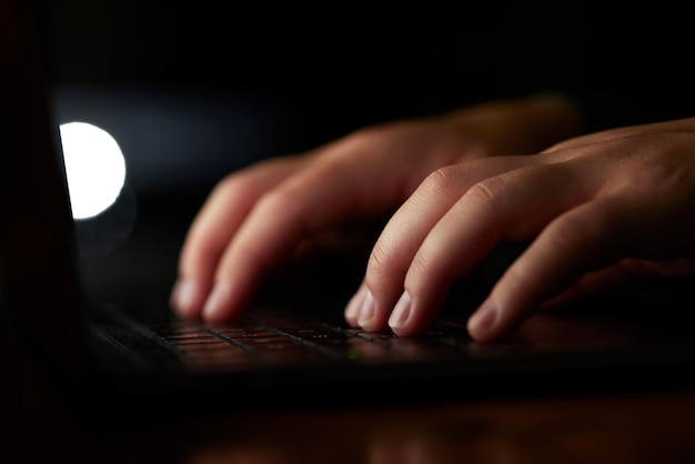 A close-up shot shows hands typing on a laptop keyboard, focusing on the fingers pressing the keys and the soft glow of the screen illuminating the hands.